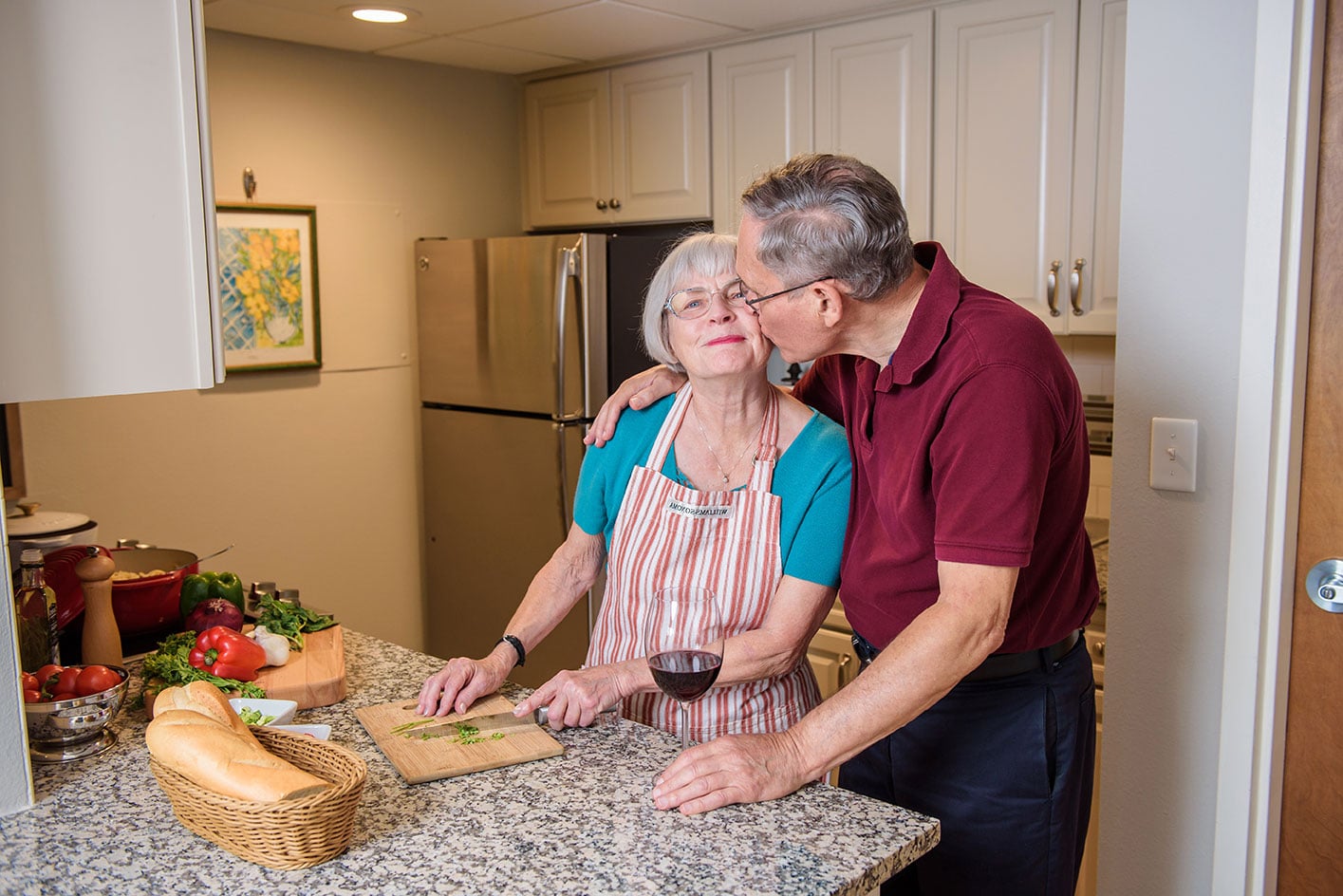 Senior man giving his wife a kiss on the check in the kitchen