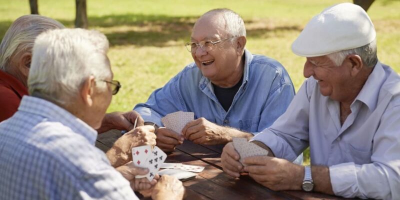 A group of older men engaged in a friendly game of cards at a picnic table, promoting senior health and wellness.