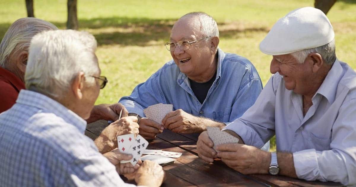 A group of older men engaged in a friendly game of cards at a picnic table, promoting senior health and wellness.