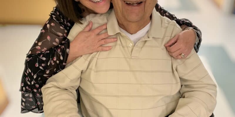 A man in a wheelchair is hugging a woman in a hospital hallway.