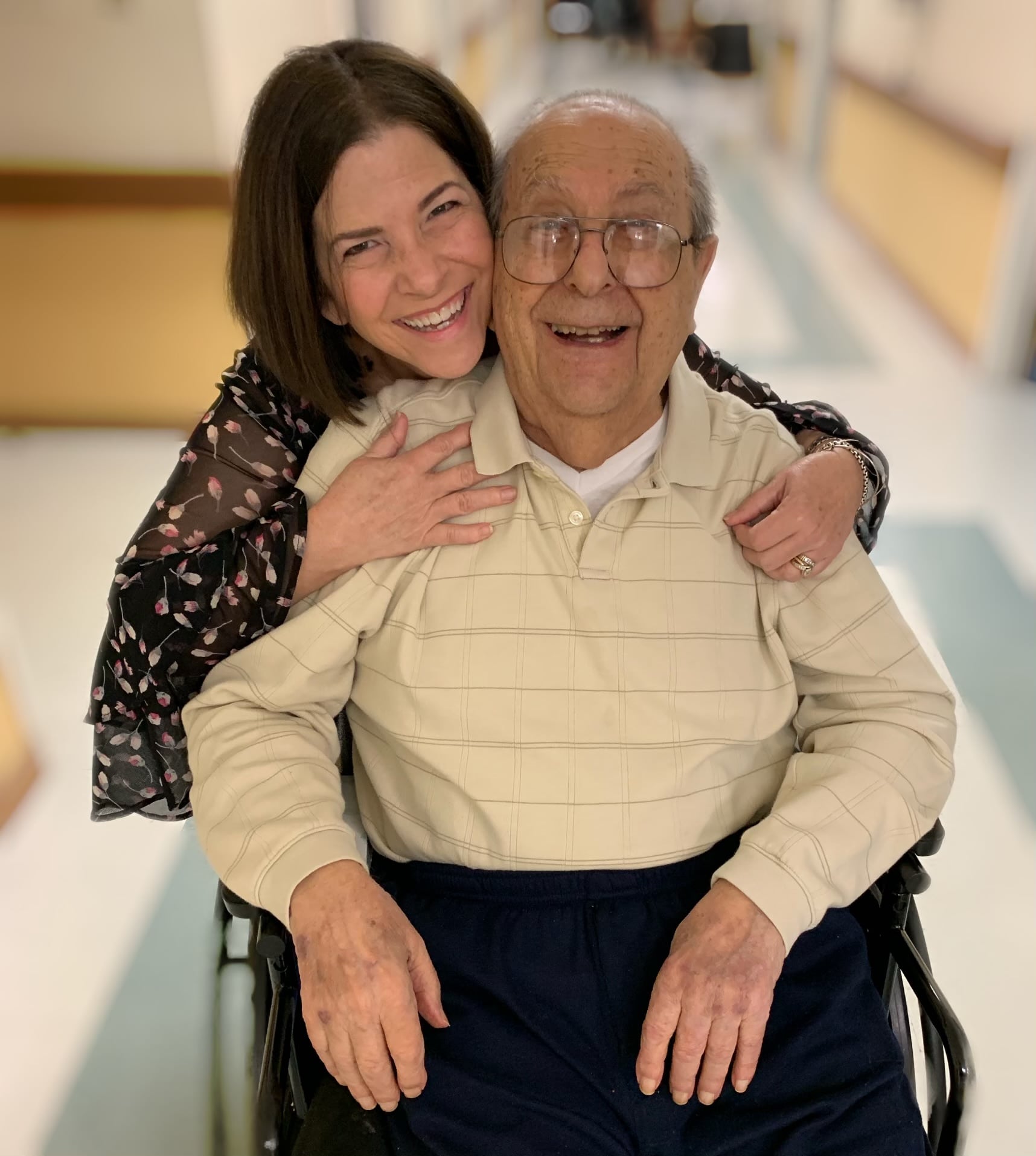 A man in a wheelchair is hugging a woman in a hospital hallway.