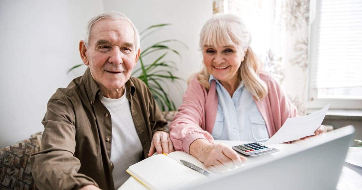 An older couple sitting at a table paying for senior living using a laptop.