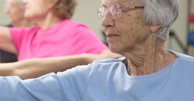 A group of older women practicing yoga in a gym.