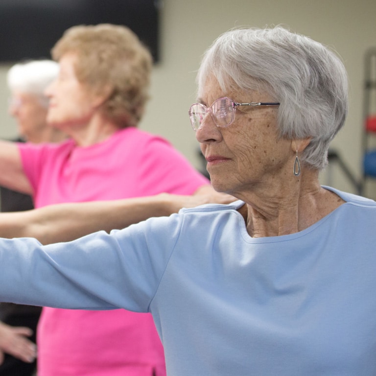 A group of older women practicing yoga in a gym.