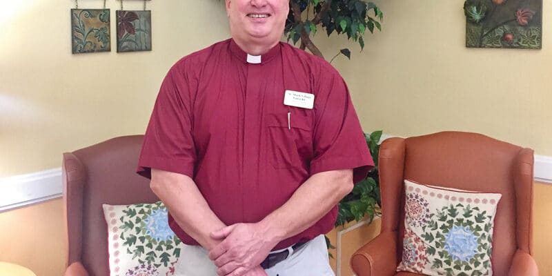 A man in a red shirt standing in front of a chair.