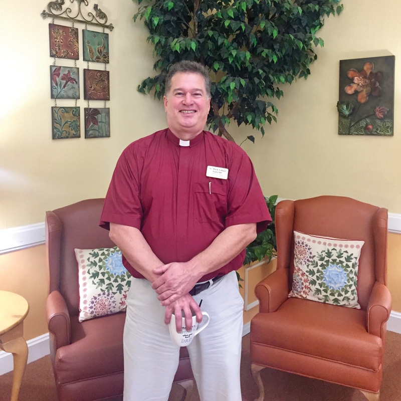 A man in a red shirt standing in front of a chair.