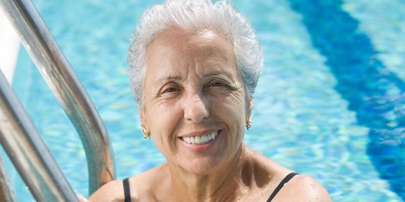 A joyful senior woman smiling in a swimming pool, enjoying the senior living amenities.