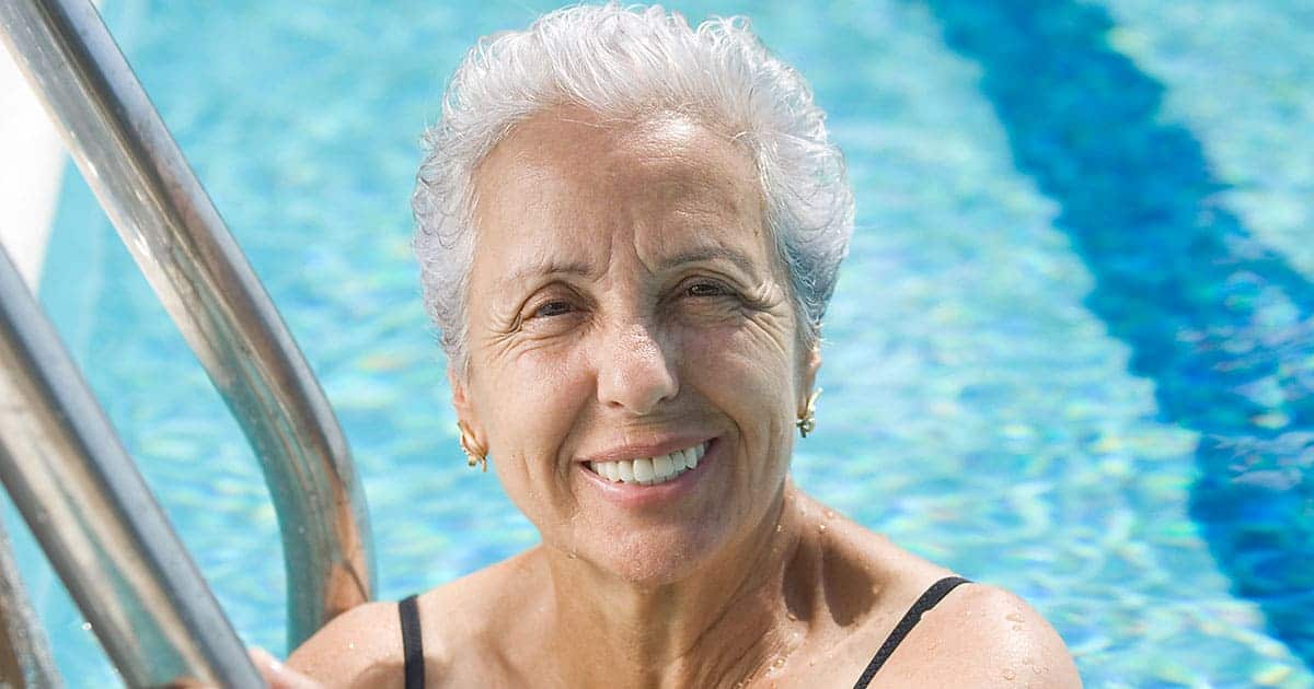 A joyful senior woman smiling in a swimming pool, enjoying the senior living amenities.