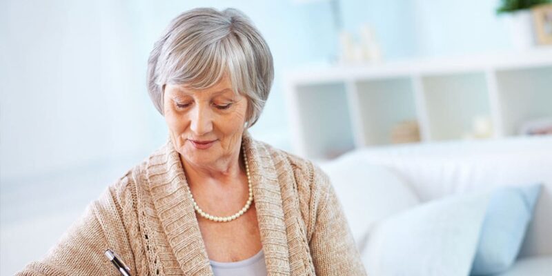 An elderly woman, engaged in her senior living search, is writing on a piece of paper.