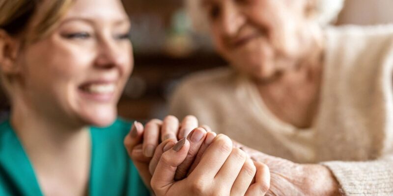 A woman is holding an elderly woman's hand.