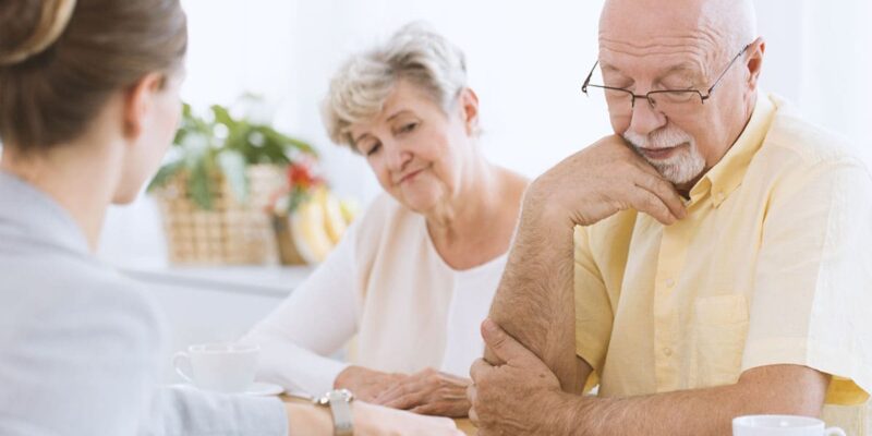 An older man is talking to an older woman at a table.