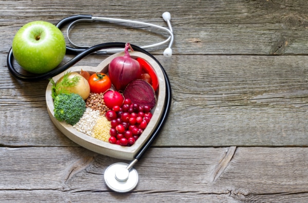 A heart shaped bowl of fruits and vegetables aimed to lower cholesterol levels, accentuated by a stethoscope.