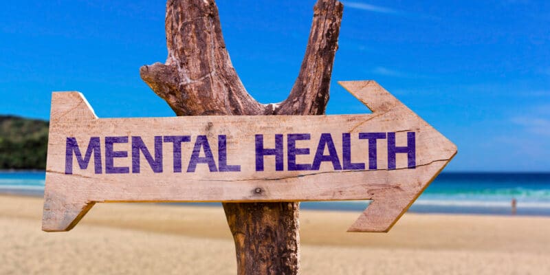 A wooden sign pointing to mental health on the beach.