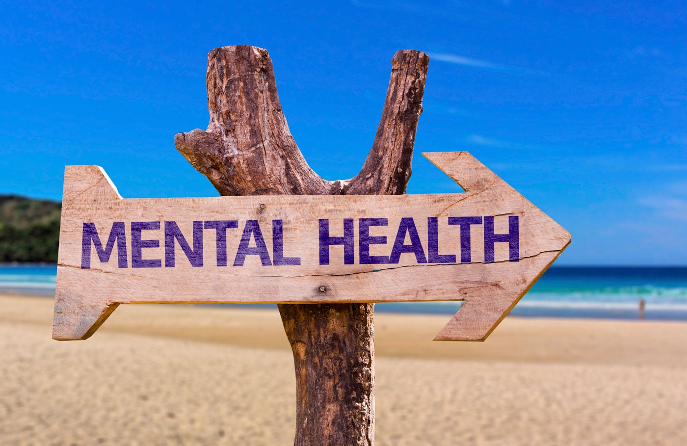 A wooden sign pointing to mental health on the beach.