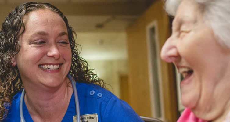 A nurse smiles with an elderly woman in a hospital room.