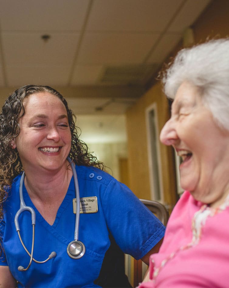 A nurse smiles with an elderly woman in a hospital room.