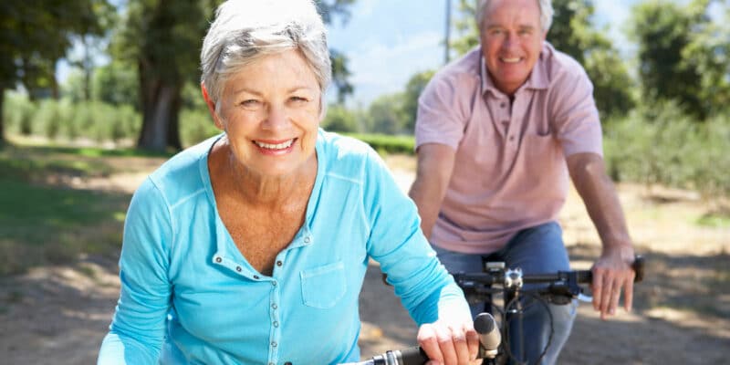 An older couple riding bikes on a country road.