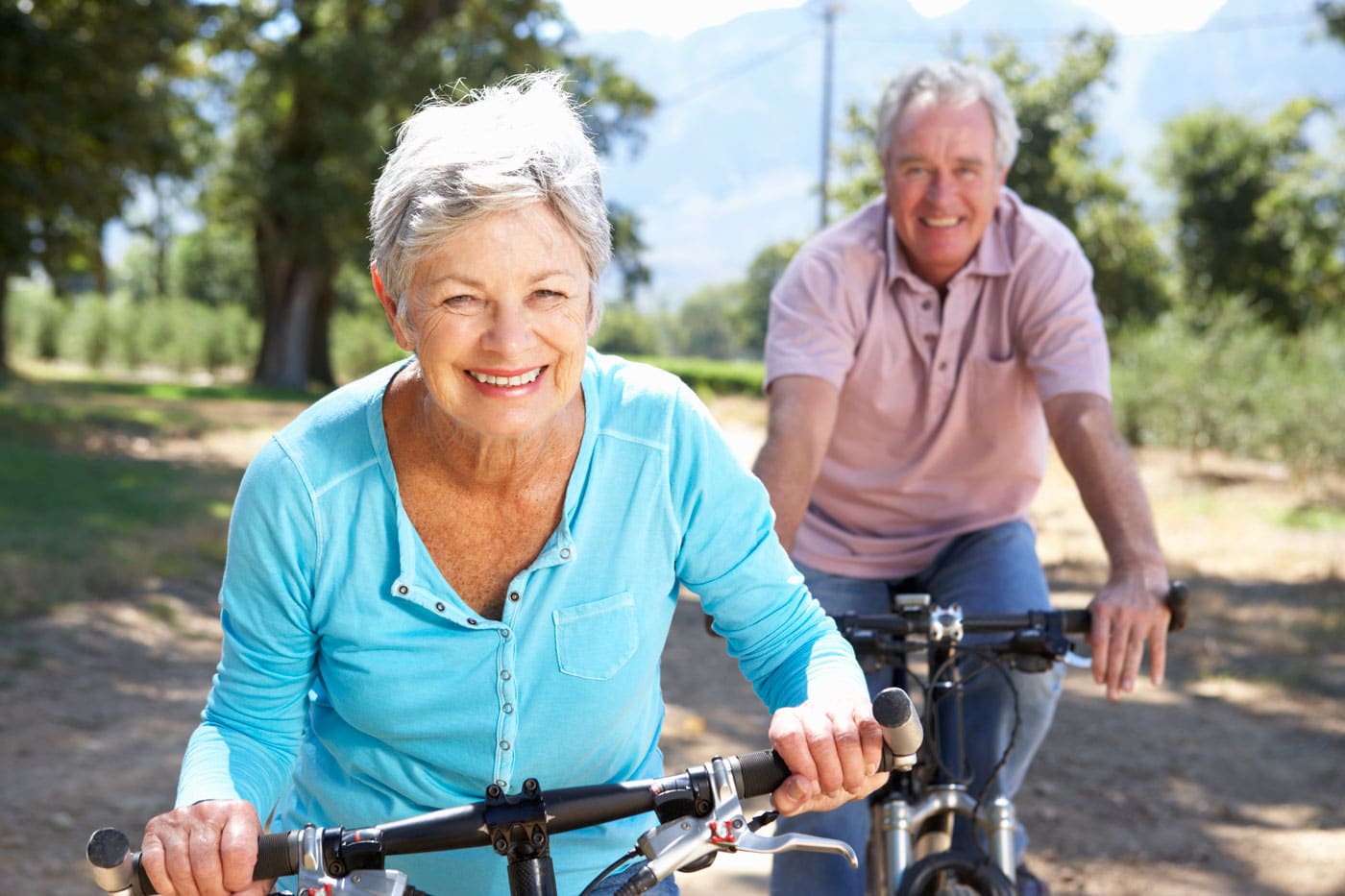 An older couple riding bikes on a country road.