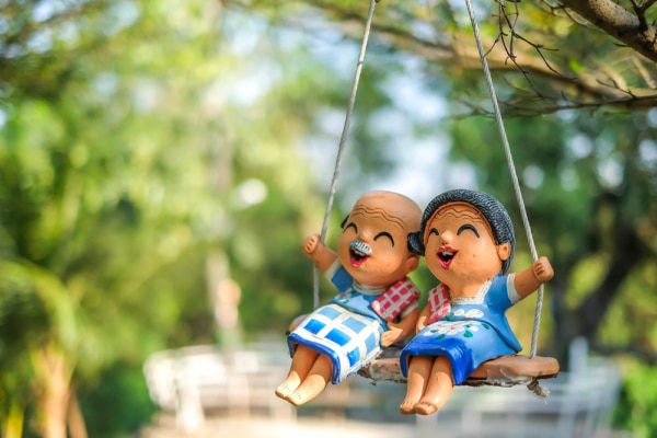 Two senior citizens figurines sitting on a swing in a park.