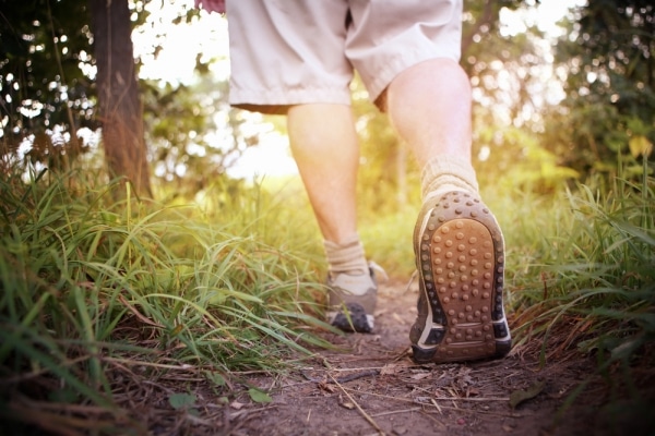 A man is walking down a trail for exercise with his shoes on.