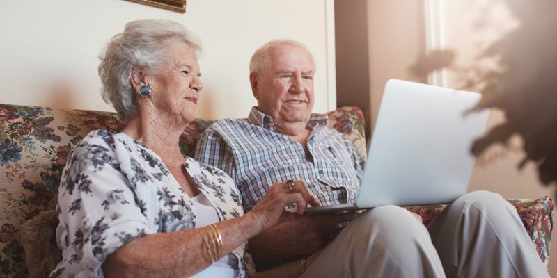An elderly couple sitting on a couch budgeting for senior living while using a laptop.