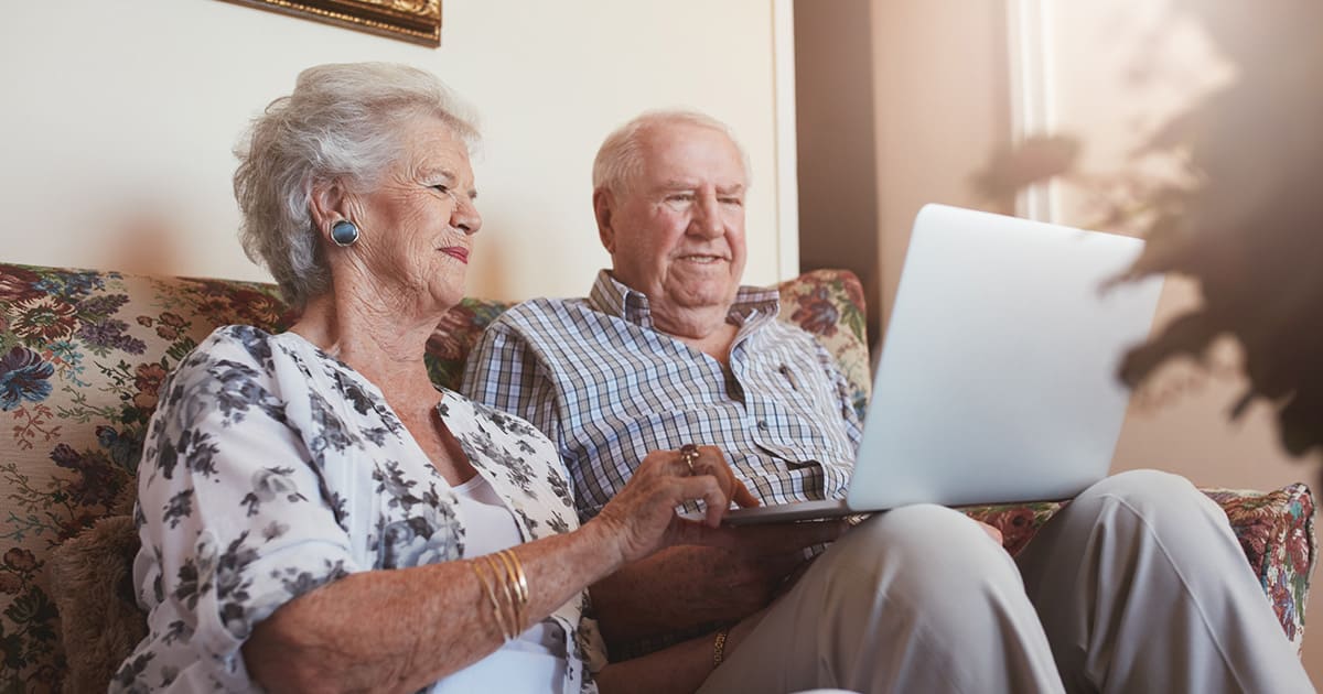 An elderly couple sitting on a couch budgeting for senior living while using a laptop.