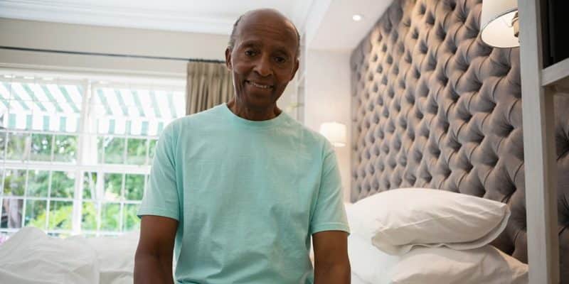 An older adult lounging on a bed in a hotel room, preparing for a restful sleep.