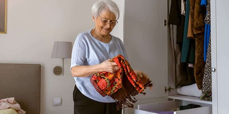 An older woman downsizing her clothes into a closet in preparation for senior living.