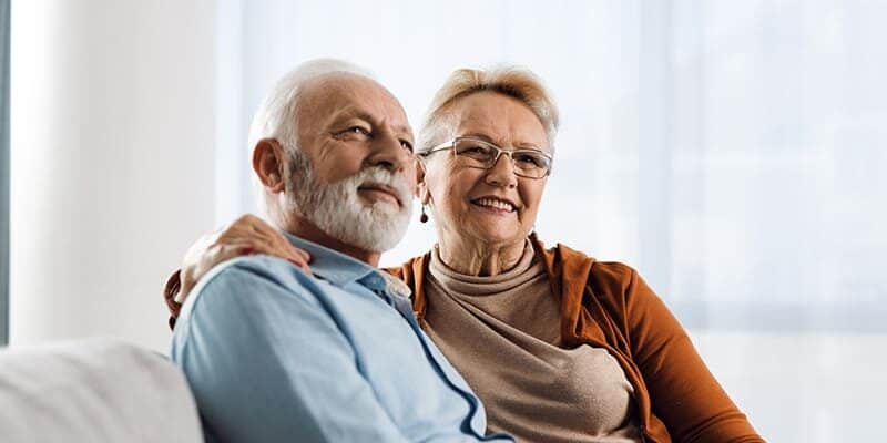 An elderly couple downsizing to senior living, sitting on a couch.