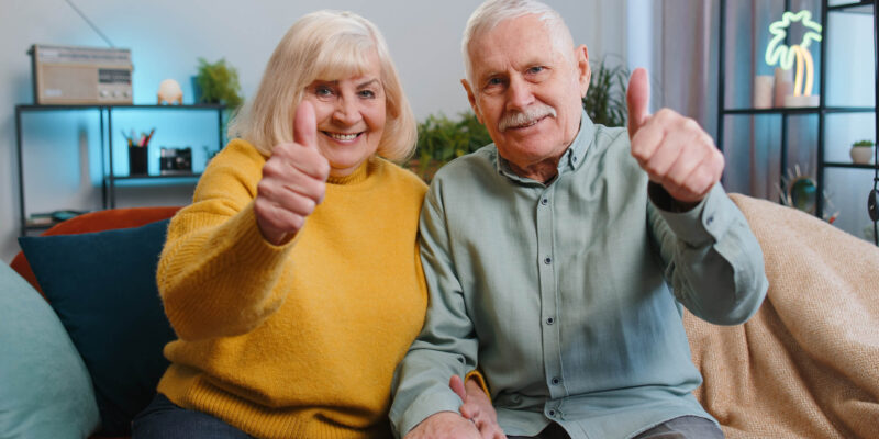Couple on couch giving a thumbs up for how CCRCs protect seniors from increasing the costs of care
