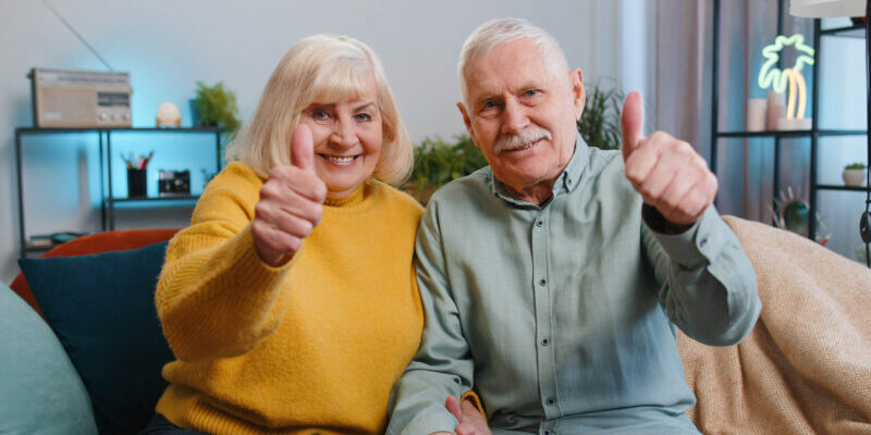 Couple on couch giving a thumbs up for how CCRCs protect seniors from increasing the costs of care