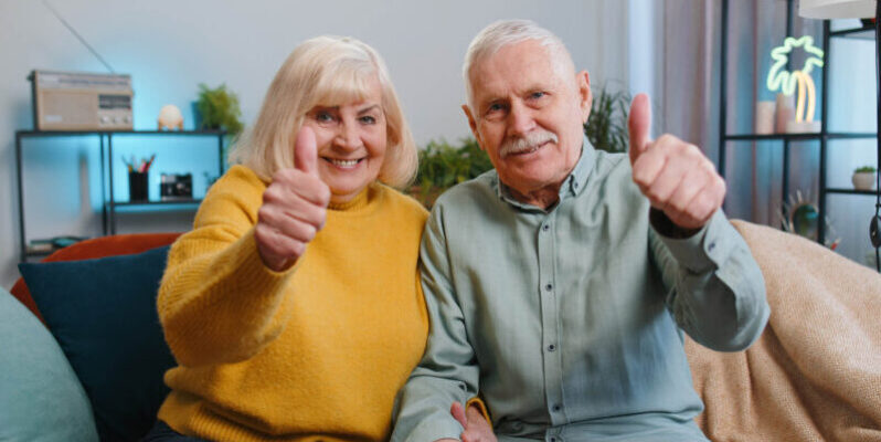 Couple on couch giving a thumbs up for how CCRCs protect seniors from increasing the costs of care