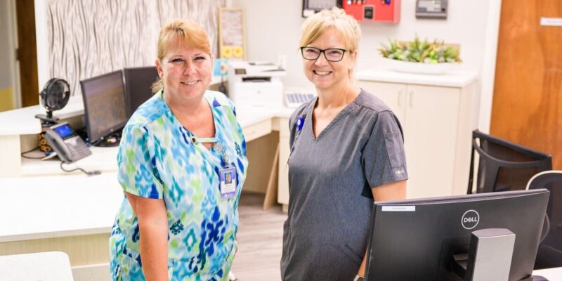 Two women standing in front of a desk in a medical office.