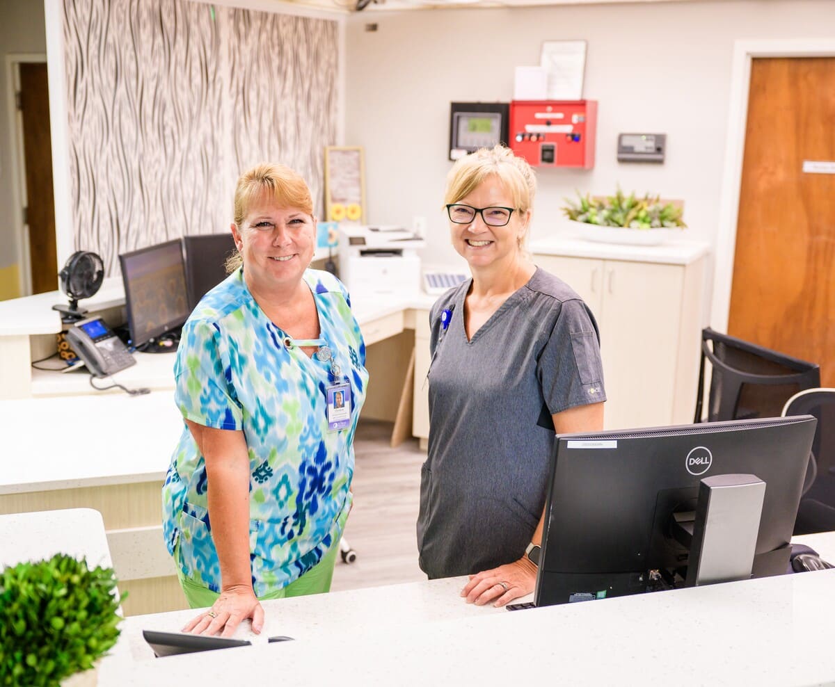 Two women standing in front of a desk in a medical office.