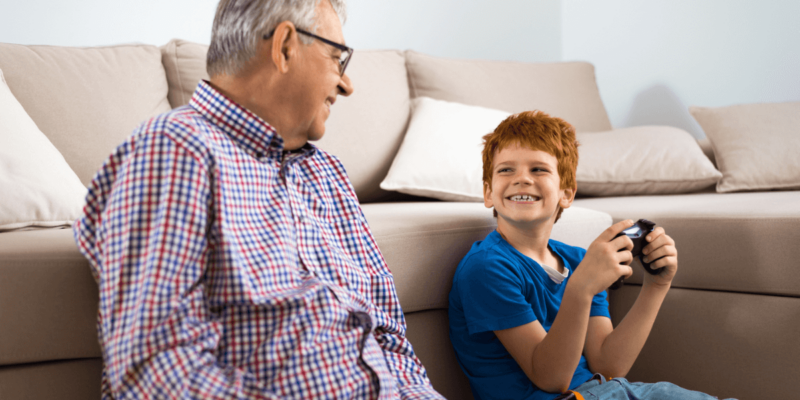 Older man sitting on the floor playing video games with his grandson