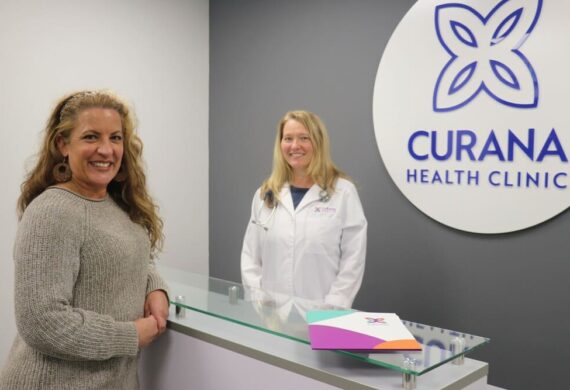 Two women standing in front of the curana health clinic sign.