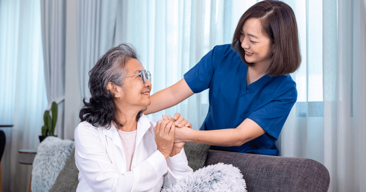 A nurse is assisting an elderly woman on the couch while incorporating elements of dance for older adults in nursing homes.