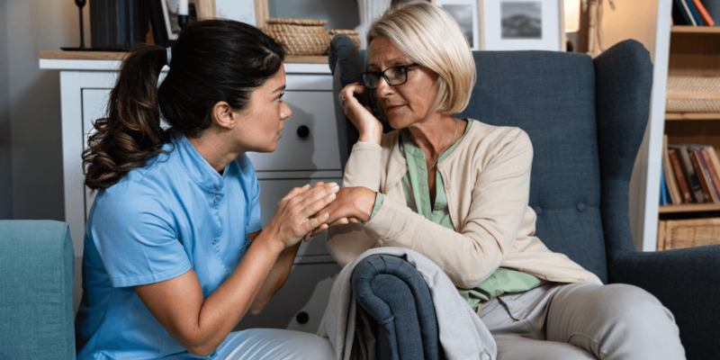 A nurse is engaging in conversation with an older woman in a chair, discussing at-home care.