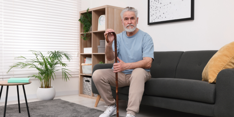 Senior man sitting on sofa with cane.