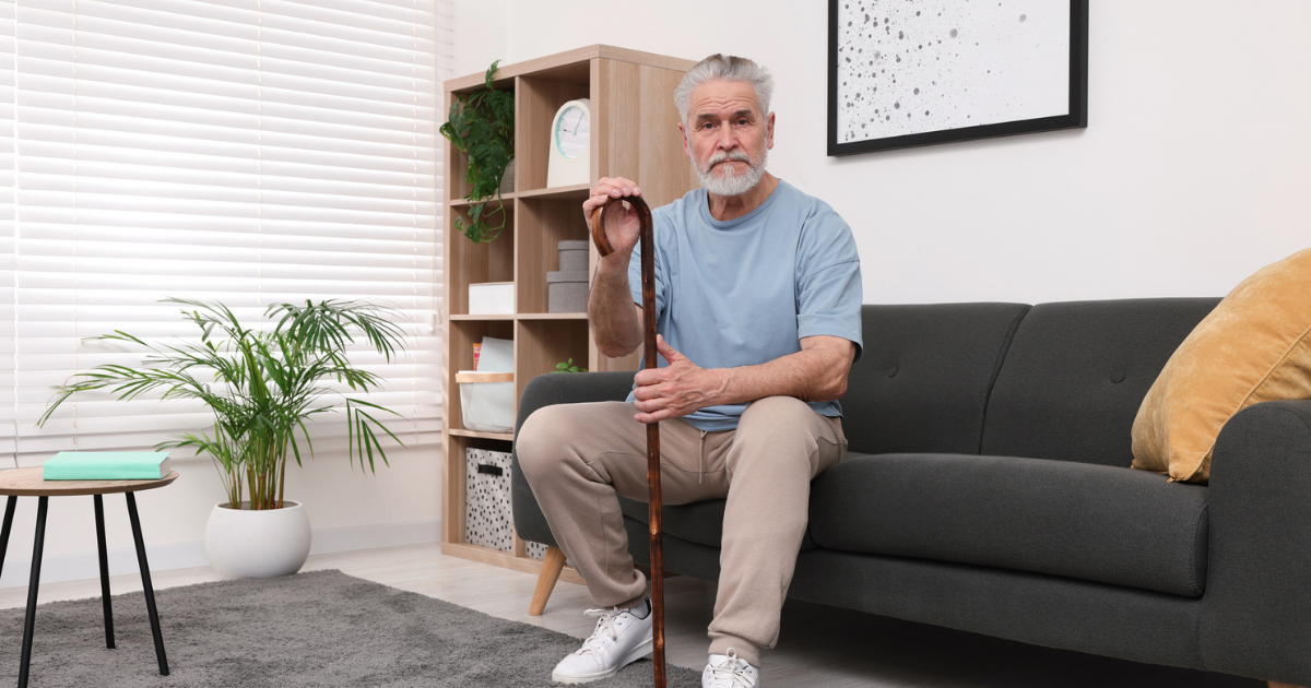 Senior man sitting on sofa with cane.