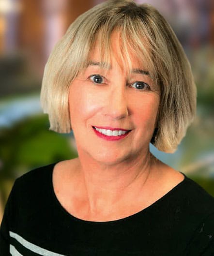 A woman with short, light blonde hair and a black top smiles at the camera against a blurred background at St. Mark Village senior living community. A woman with short, light blonde hair and a black top smiles at the camera against a blurred background at St. Mark Village senior living community.