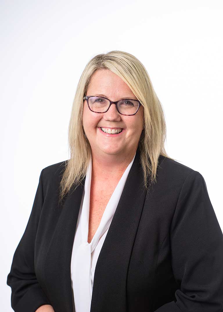 A woman with blonde hair and glasses, wearing a black blazer and white blouse, smiles at the camera against a plain white background, reflecting the welcoming spirit of senior living at St. Mark Village. A woman with blonde hair and glasses, wearing a black blazer and white blouse, smiles at the camera against a plain white background, reflecting the welcoming spirit of senior living at St. Mark Village.