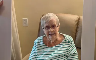 An elderly woman sits in a chair, smiling, holding a large frame that says "St. Mark Village" at the top and "I DID IT!!!" at the bottom, celebrating her vibrant life in senior living.