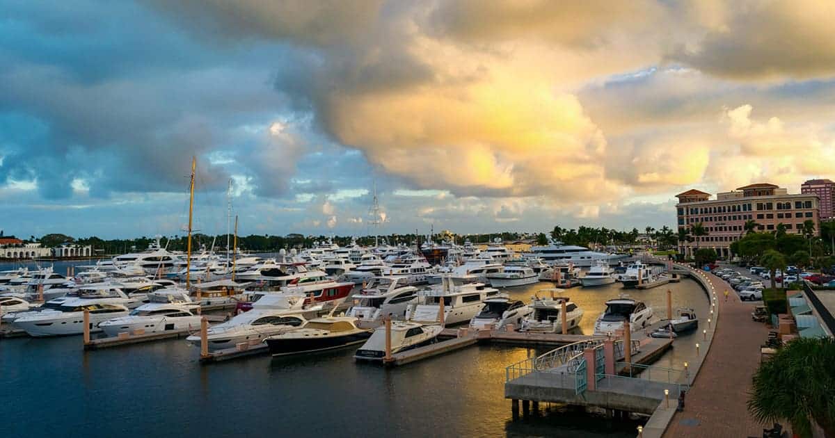 Dozens of yachts and boats docked at a large marina under a partly cloudy sky, with a walkway and buildings in the background, set near the vibrant community of St. Mark Village senior living.