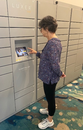 A woman at St. Mark Village interacts with a touchscreen on a Luxer One package locker system in front of a wall of locked compartments, enhancing convenience and security in this senior living community. A woman at St. Mark Village interacts with a touchscreen on a Luxer One package locker system in front of a wall of locked compartments, enhancing convenience and security in this senior living community.
