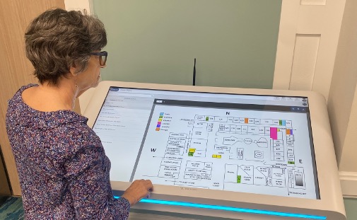 A woman explores a digital floor plan on a large touchscreen display, navigating the senior living options available at St. Mark Village.