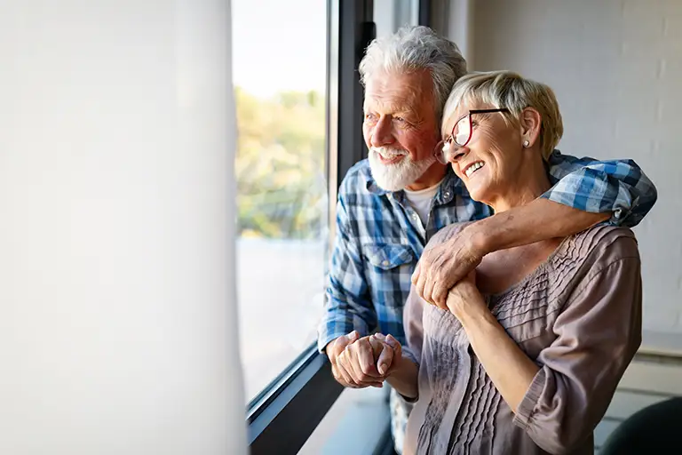 An older man and woman stand by a window at St. Mark Village, smiling and embracing while holding hands. Natural light streams in from outside, capturing the warmth of senior living. An older man and woman stand by a window at St. Mark Village, smiling and embracing while holding hands. Natural light streams in from outside, capturing the warmth of senior living.