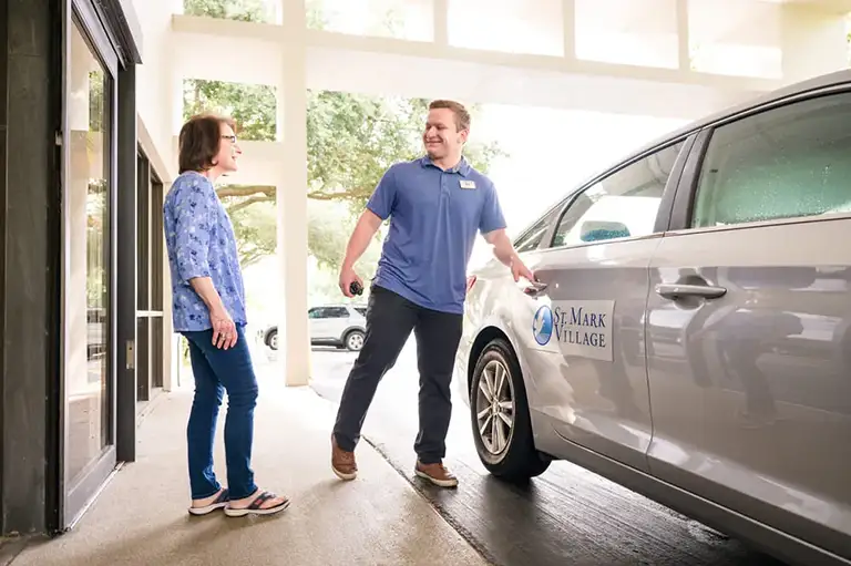 A man opens the door of a St. Mark Village car for a woman standing nearby under a covered walkway, reflecting the welcoming spirit of senior living at St. Mark Village. A man opens the door of a St. Mark Village car for a woman standing nearby under a covered walkway, reflecting the welcoming spirit of senior living at St. Mark Village.