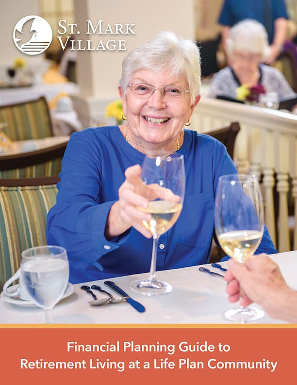 An elderly woman smiles and raises a glass of white wine while dining at St. Mark Village, a vibrant senior living community with other seniors enjoying themselves in the background.
