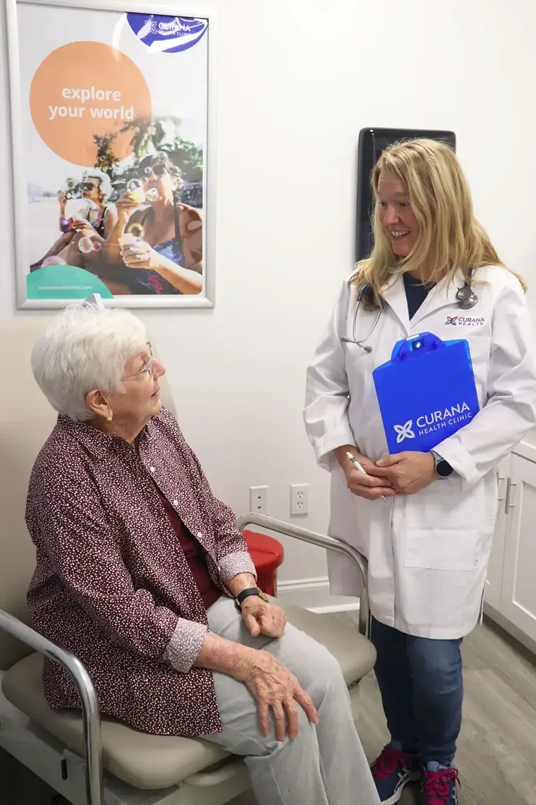 A doctor in a white coat holds a blue clipboard while talking to an elderly woman seated in a medical exam room at St. Mark Village, a trusted senior living community. A doctor in a white coat holds a blue clipboard while talking to an elderly woman seated in a medical exam room at St. Mark Village, a trusted senior living community.
